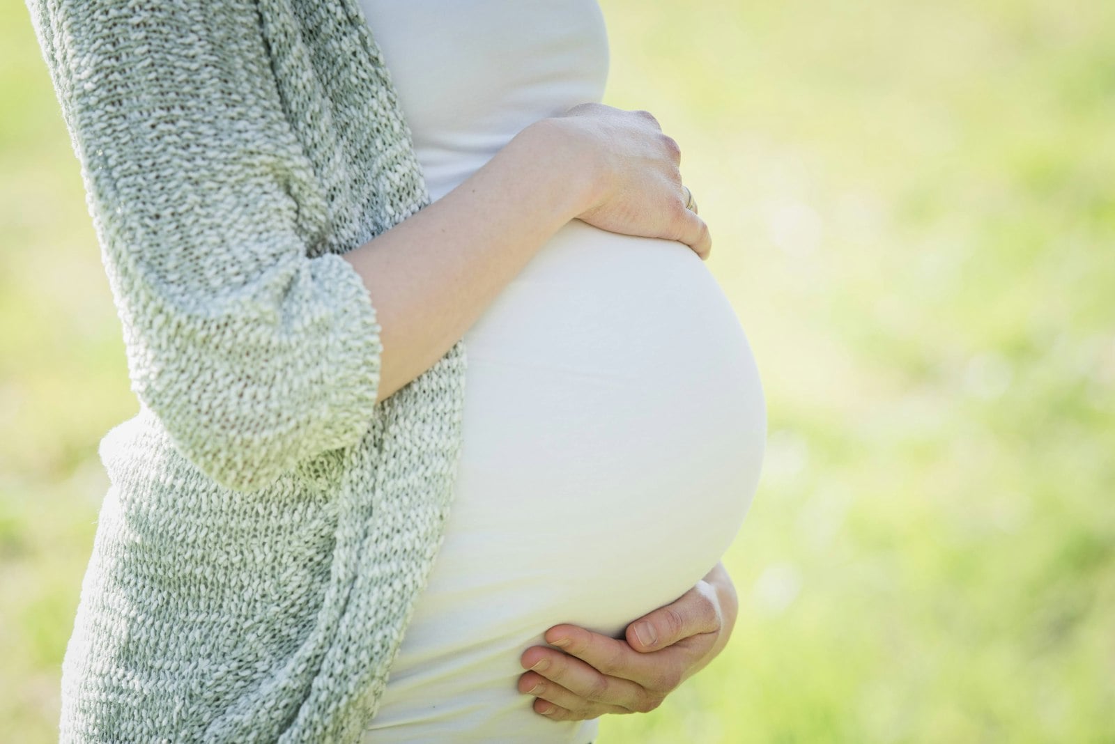 Gestante segurando a barriga com as duas mãos, luz natural